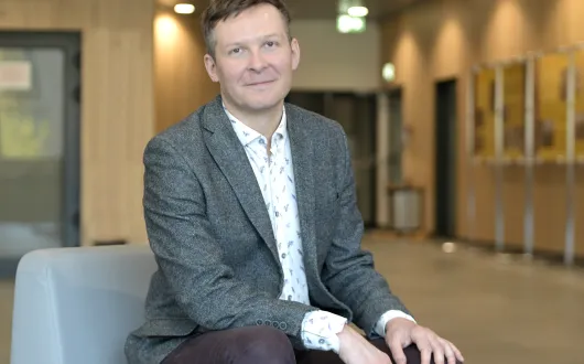 mężczyzna w średnim wieku uśmiecha się na zdjęciu, siedząc z dłońmi na kolanach opartymi