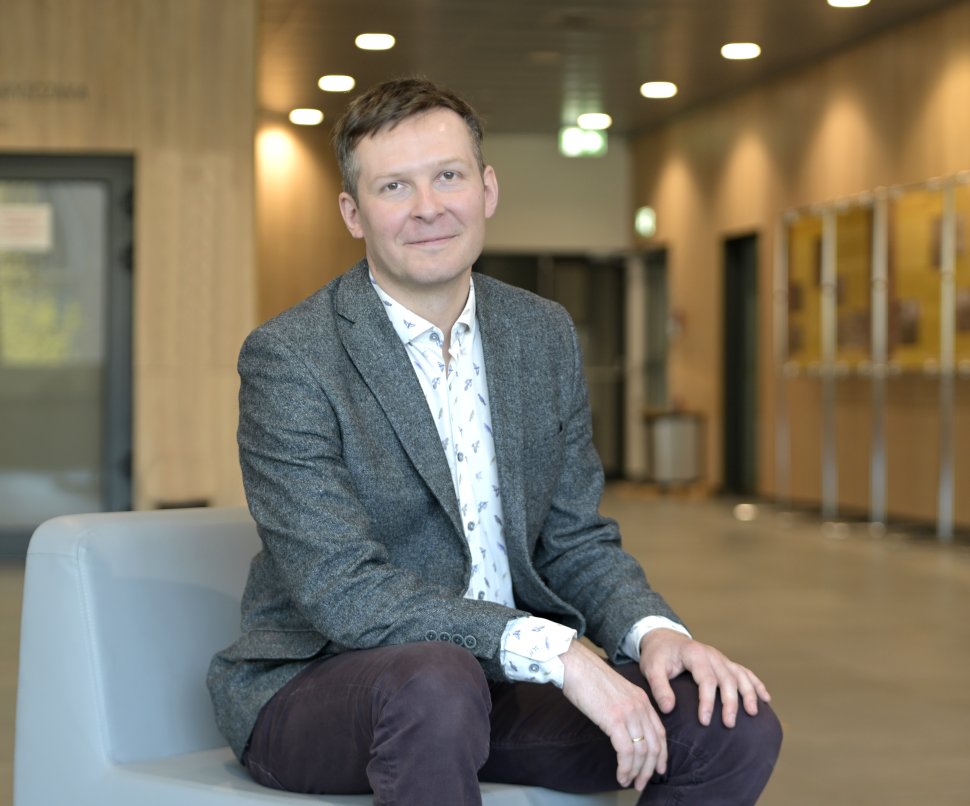 mężczyzna w średnim wieku uśmiecha się na zdjęciu, siedząc z dłońmi na kolanach opartymi