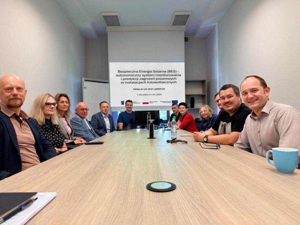 Grupa ludzi, siedząca przy stole, związana z projektem dotyczącym bezpieczeństwa farm fotowoltaicznych