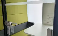 Zdjęcie budki akustycznej dla studentów z antracytową obudową, zielonym wnętrzem, białym blatem stolika.