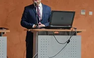 dr hab. inż. Przemysław Tabaka stoi w garniturze przy mównicy i przemawiając do gości otwiera Konferencję. 