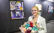 Pani dr Aleksandra Królak z bukietem w dłoniach na tle swojej wystawy fotografii w Galerii Pod Napięciem. 