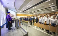 Prorektor oraz Kolegium Dziekańskie w auli stoją na baczność do hymnu Polski. 